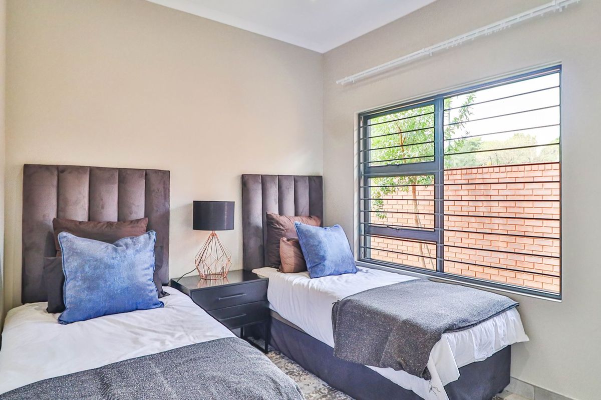 A well-lit bedroom featuring a large window with integrated security bars, neutral wall finishes, and a clean, modern aesthetic.