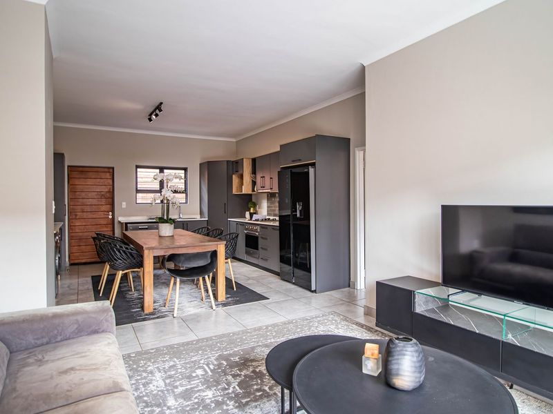 Open-plan living and dining area featuring a modern kitchen with dark cabinetry, tiled flooring, and integrated appliances.