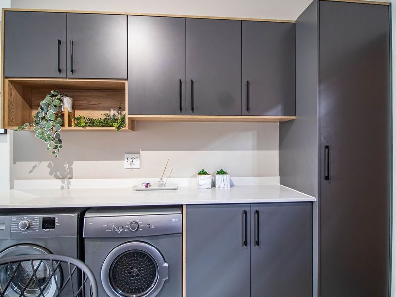 Modern laundry area featuring sleek grey cabinetry, white stone countertops, and dedicated spaces for under-counter appliances.