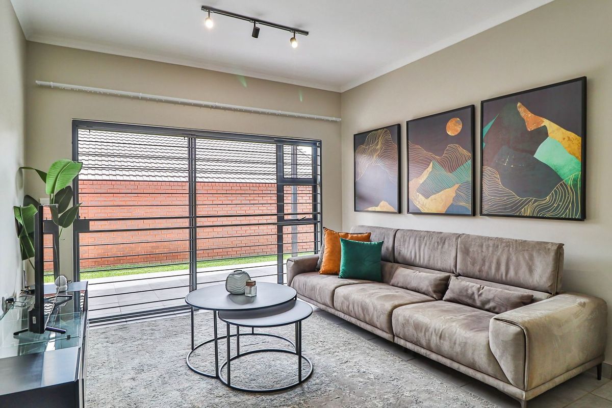 A bright living room featuring large sliding glass doors that open to an outdoor patio area, complemented by modern track lighting.