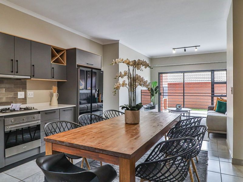 Open-plan living area featuring a modern kitchen with grey cabinetry, built-in oven and hob, flowing into a dining space with access to a rear patio.