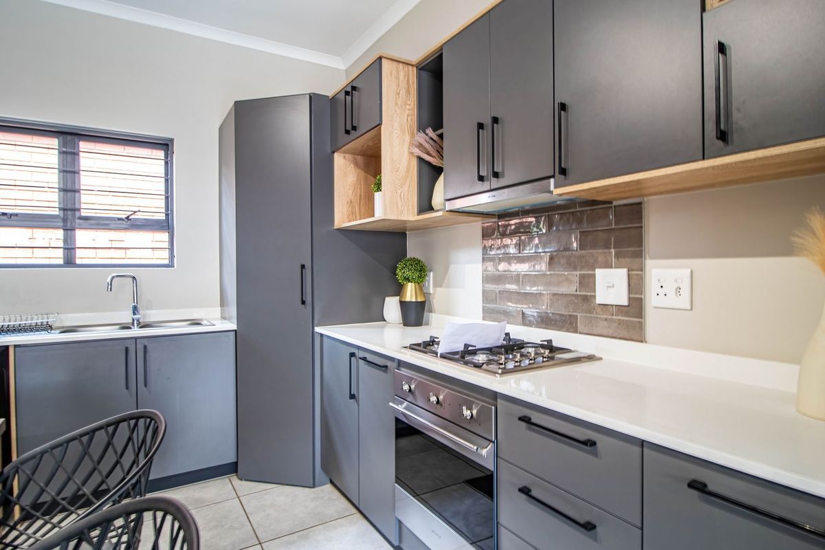 Modern kitchen featuring dark grey cabinetry, light wood accents, stone countertops, a built-in oven, gas hob, and a tiled backsplash.