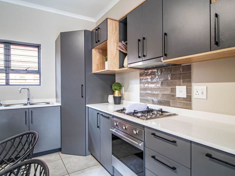 Modern kitchen featuring dark grey cabinetry, light wood accents, stone countertops, a built-in oven, gas hob, and a tiled backsplash.