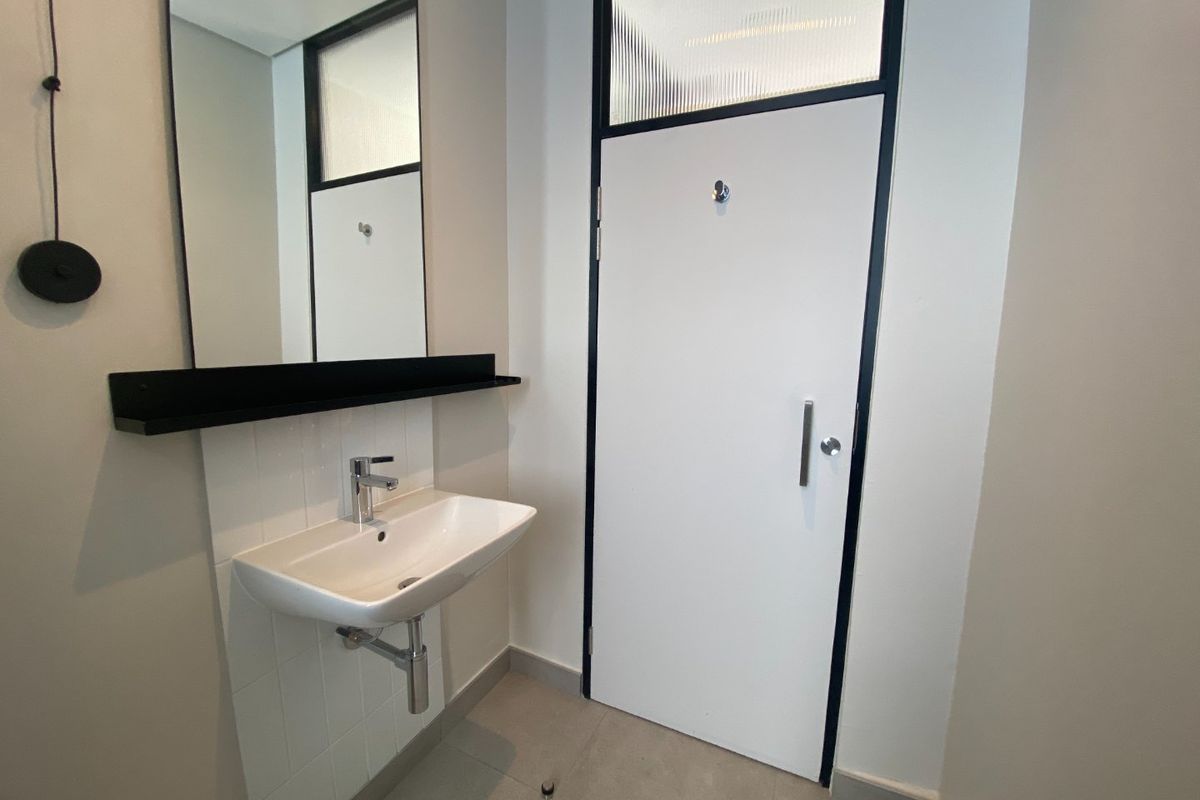 A modern bathroom featuring a wall-mounted basin, sleek black shelving, a large mirror, and a contemporary door with a reeded glass transom window.
