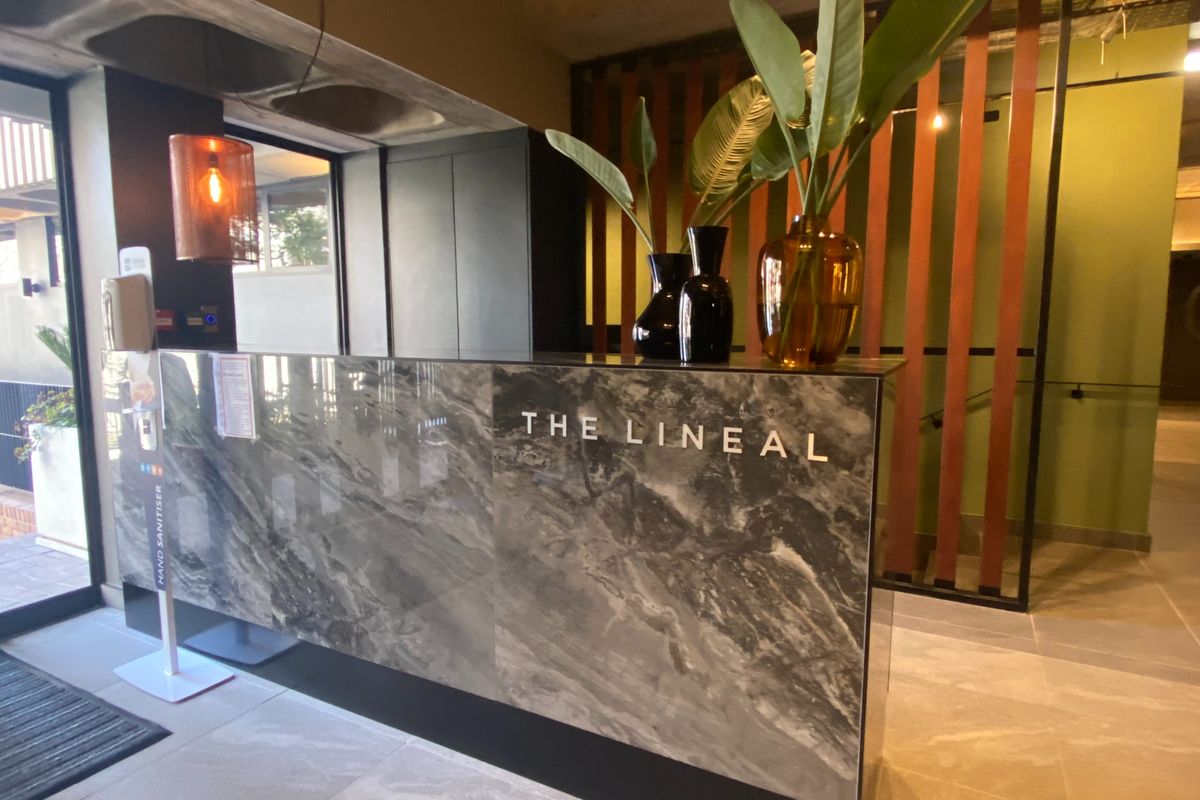 Modern reception area featuring a sleek marble-finish concierge desk, industrial-style exposed concrete ceiling, and decorative timber slat room dividers.
