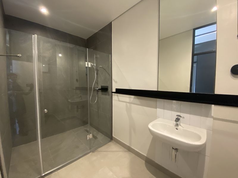 Modern bathroom featuring a glass-enclosed walk-in shower with dark grey tiling, a wall-mounted basin, and a large vanity mirror.
