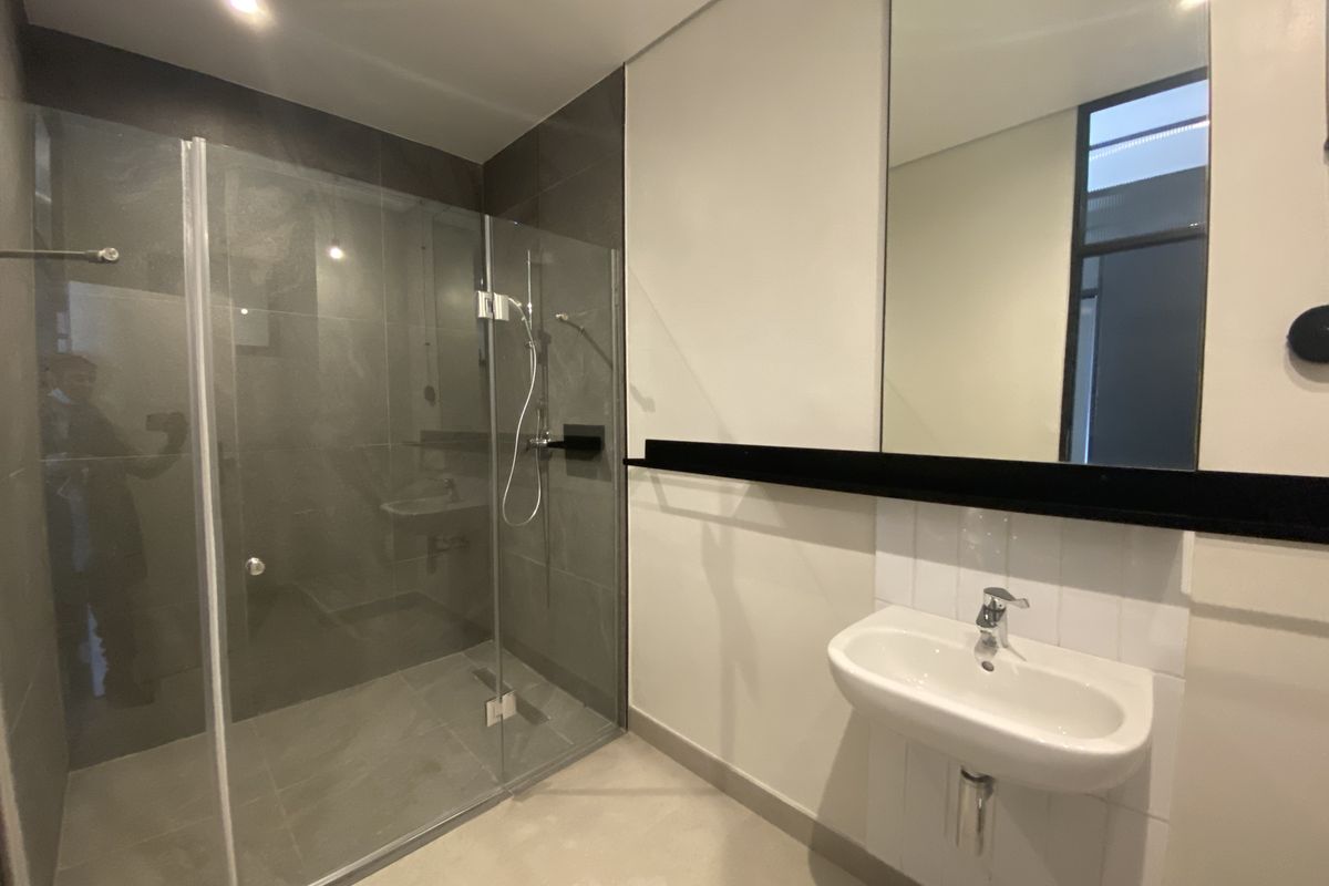 Modern bathroom featuring a glass-enclosed walk-in shower with dark grey tiling, a wall-mounted basin, and a large vanity mirror.