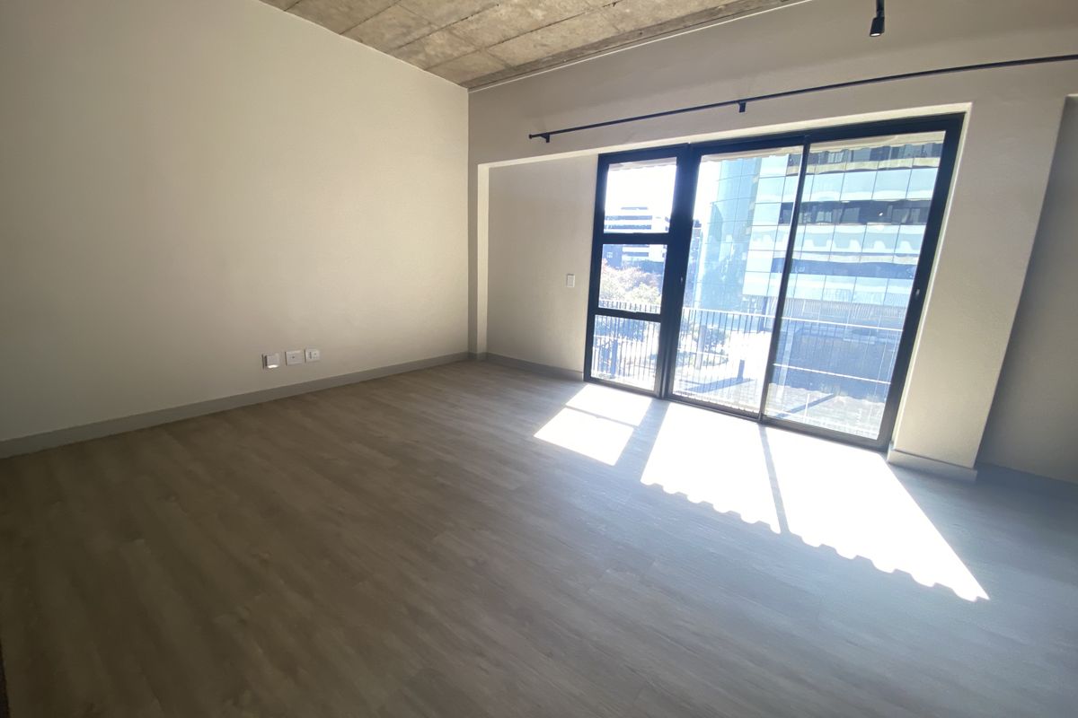 A bright, empty living room featuring modern wood-look flooring, an exposed concrete ceiling, and large sliding glass doors leading to a balcony.