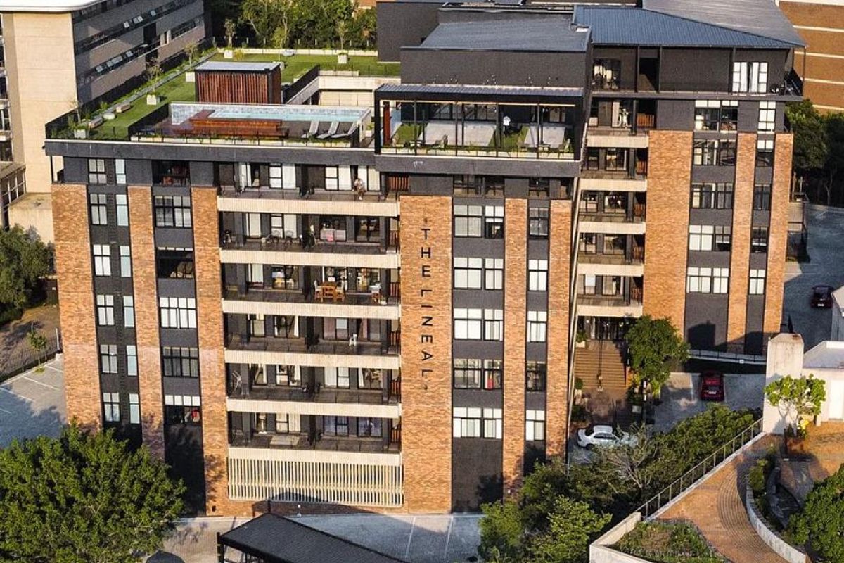Aerial view of The Lineal apartment complex, showcasing its modern brick and dark facade, rooftop amenities, and secure gated entrance.