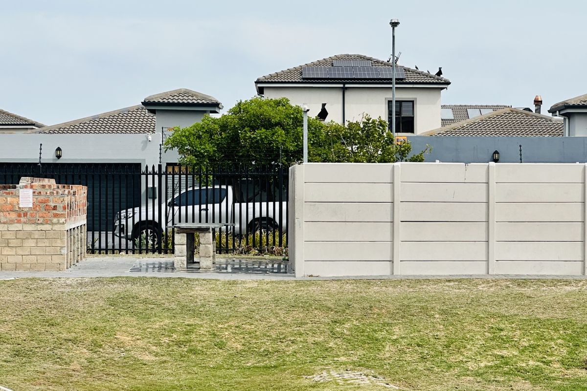 Outdoor area featuring a brick braai, concrete table, and perimeter walling, set against a residential backdrop with solar panels visible on the roof.