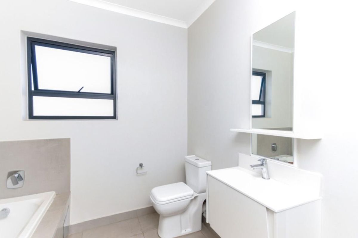 A clean, modern bathroom featuring a white vanity with integrated basin, a wall-mounted mirror, a toilet, and a bathtub with neutral tiling.