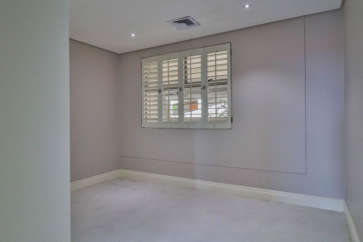 A clean, neutral-toned bedroom featuring fitted plantation shutters, recessed downlighting, and integrated air conditioning vent.