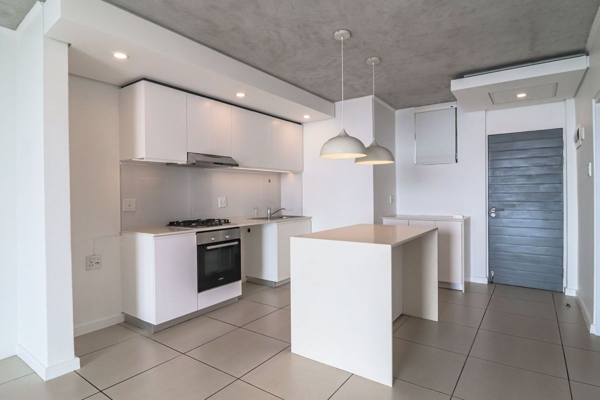 Modern kitchen featuring white cabinetry, stone countertops, a central island, built-in oven, gas hob, and extractor fan, set against a contemporary concrete-look ceiling.