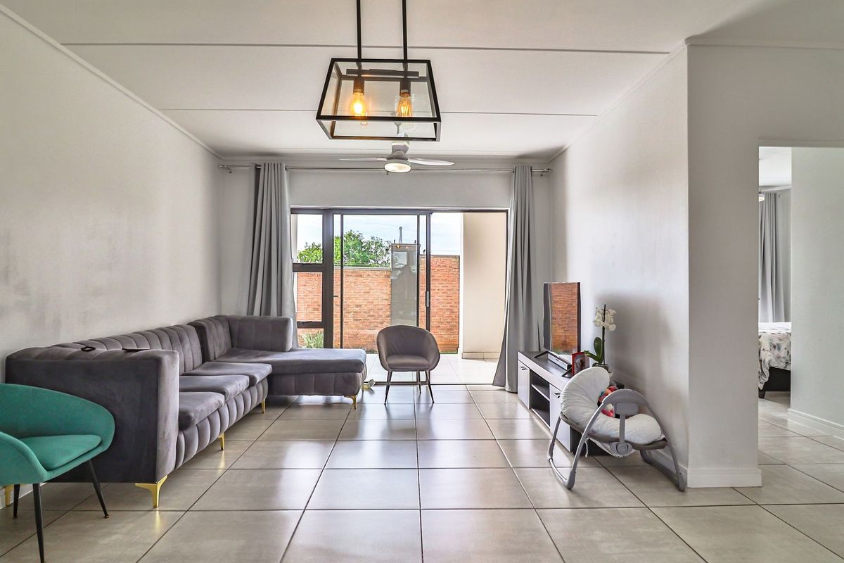 A bright and spacious living room featuring large format floor tiles, a modern pendant light, and a sliding glass door leading to an outdoor area.