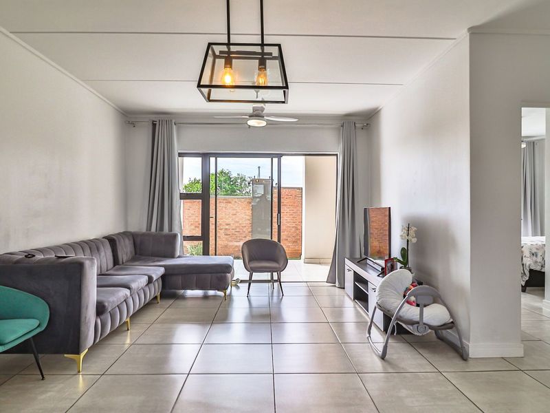 A bright and spacious living room featuring large format floor tiles, a modern pendant light, and a sliding glass door leading to an outdoor area.