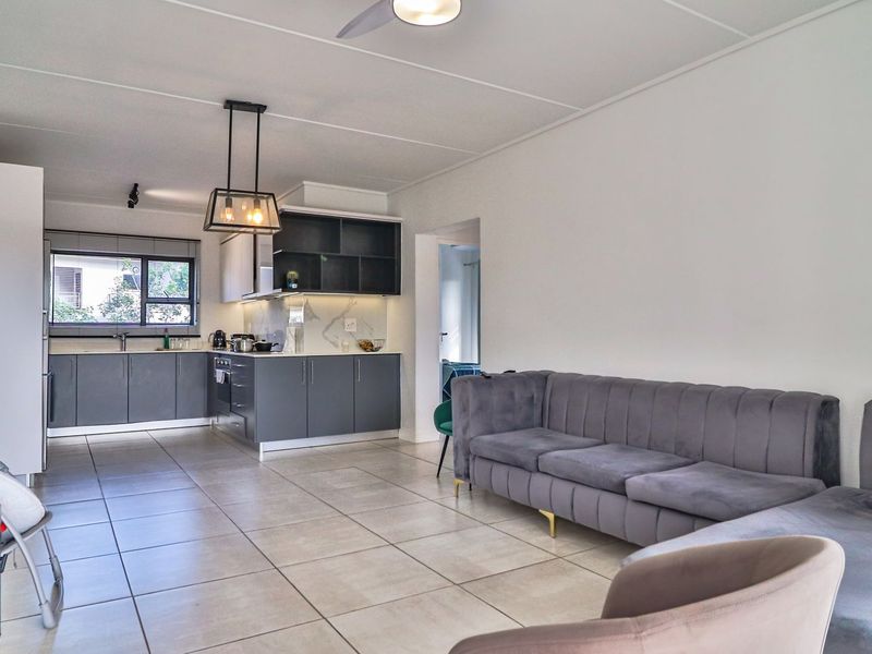 Modern open-plan living area featuring a contemporary kitchen with dark cabinetry, stone countertops, and neutral tiled flooring throughout the combined space.