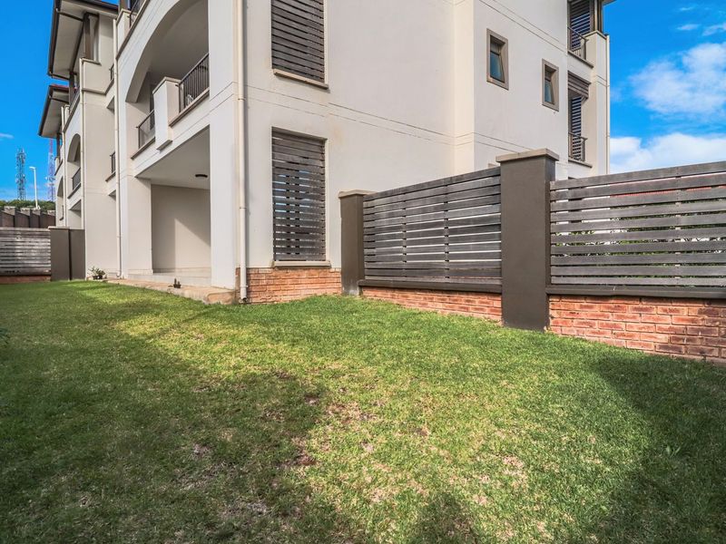 A well-maintained rear garden area featuring a lawn, brick and timber boundary fencing, and access to a covered patio.