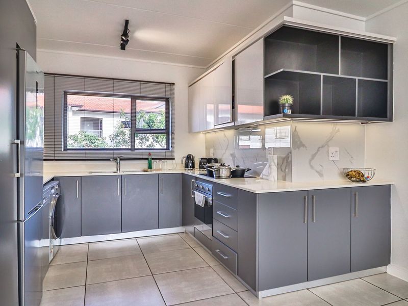 Modern kitchen featuring sleek grey cabinetry, stone countertops, marble-look splashback, integrated oven, and hob, with ample storage and under-cabinet lighting.