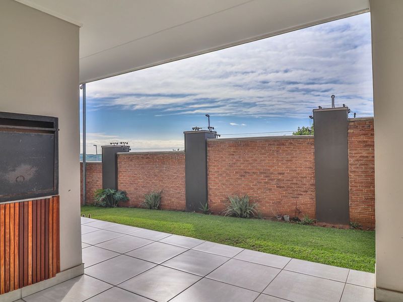 A covered patio featuring tiled flooring and a built-in braai, overlooking a private garden with a brick boundary wall.