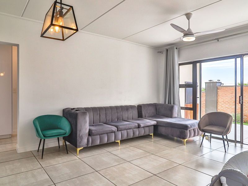 A bright living room featuring large format floor tiles, a modern ceiling fan, and sliding glass doors providing access to an outdoor patio area.