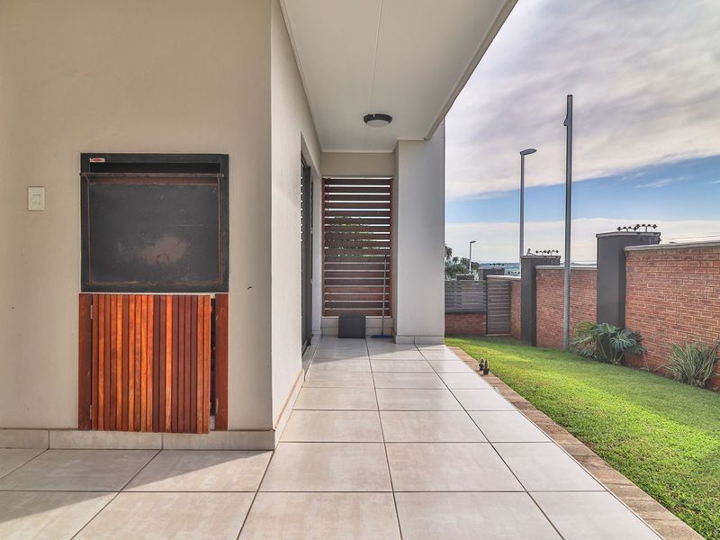 A covered patio featuring tiled flooring and a built-in braai, overlooking a private garden area with brick boundary walls.