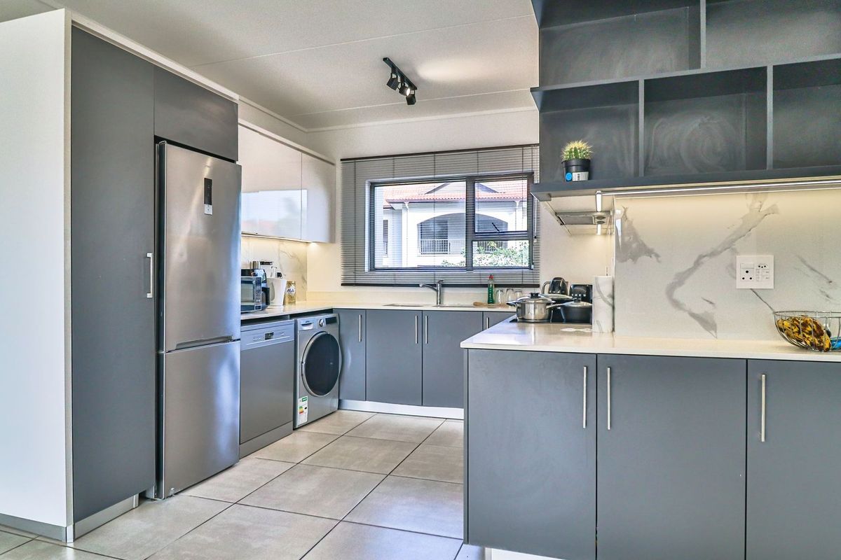 Modern kitchen featuring sleek grey cabinetry, stone countertops, marble-look splashback, integrated sink, and contemporary track lighting with tiled flooring.