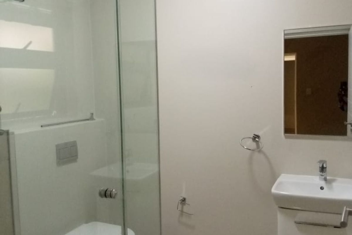 A functional bathroom featuring a glass-enclosed shower, wall-mounted toilet, and a modern vanity basin with a mirror.