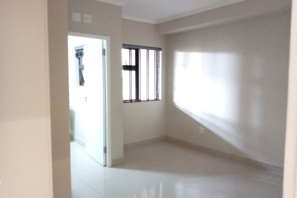 A bright, empty bedroom featuring neutral tiled flooring, clean walls, and a window fitted with horizontal blinds, offering a versatile living space.