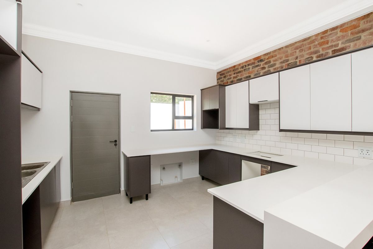 Modern kitchen featuring two-tone cabinetry, white stone countertops, subway tile backsplash, and an exposed brick accent wall.