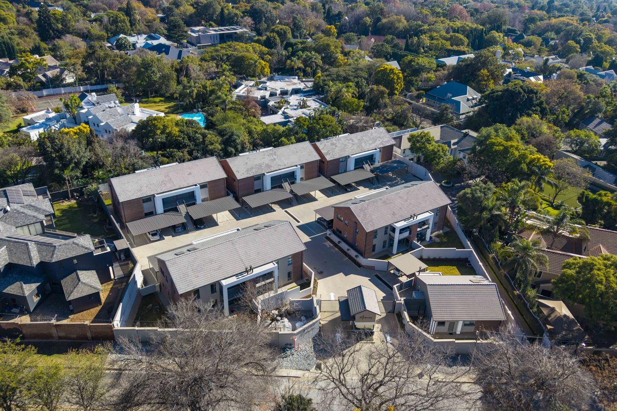 Aerial view of a modern apartment complex featuring multiple residential buildings, paved driveways, covered parking bays, and landscaped surroundings.