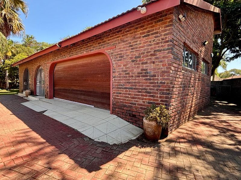 A detached brick garage featuring a large automated door, tiled roof, and paved driveway access within a landscaped garden setting.