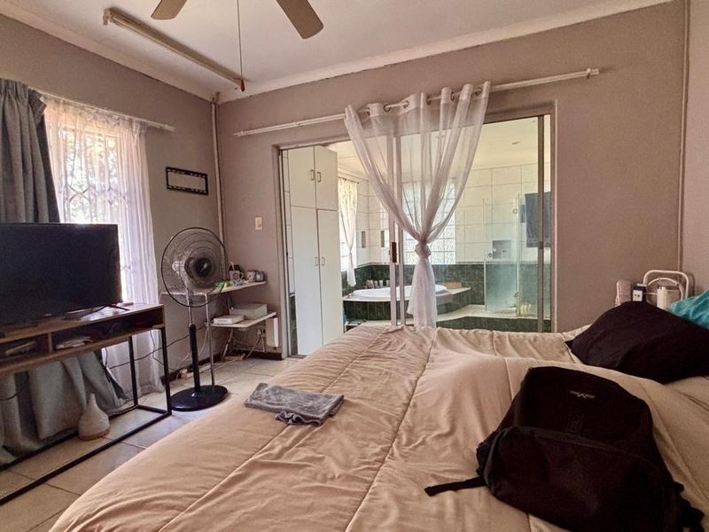 Spacious bedroom featuring tiled flooring, a ceiling fan, and direct access to an en-suite bathroom through sliding glass doors.