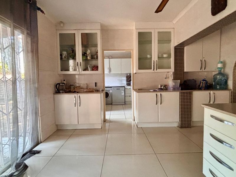 A functional kitchen featuring white cabinetry, glass-fronted display units, and tiled flooring, with an adjacent scullery area visible through the doorway.