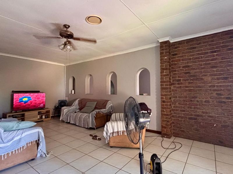 Spacious living room featuring an exposed brick accent wall, tiled flooring, and decorative arched wall niches.