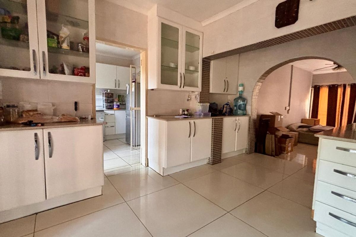 A functional kitchen featuring white built-in cabinetry, tiled flooring, and an open archway leading to the adjacent living area.