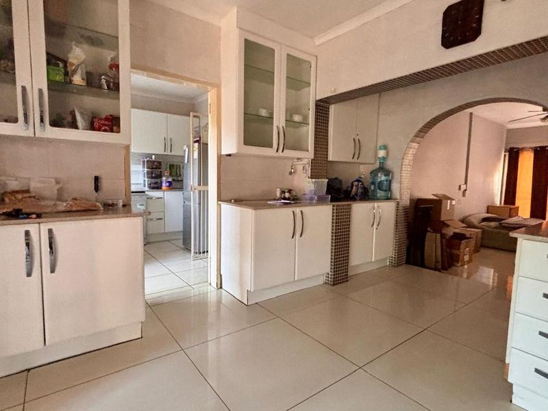 A functional kitchen featuring white built-in cabinetry, tiled flooring, and an open archway leading to the adjacent living area.