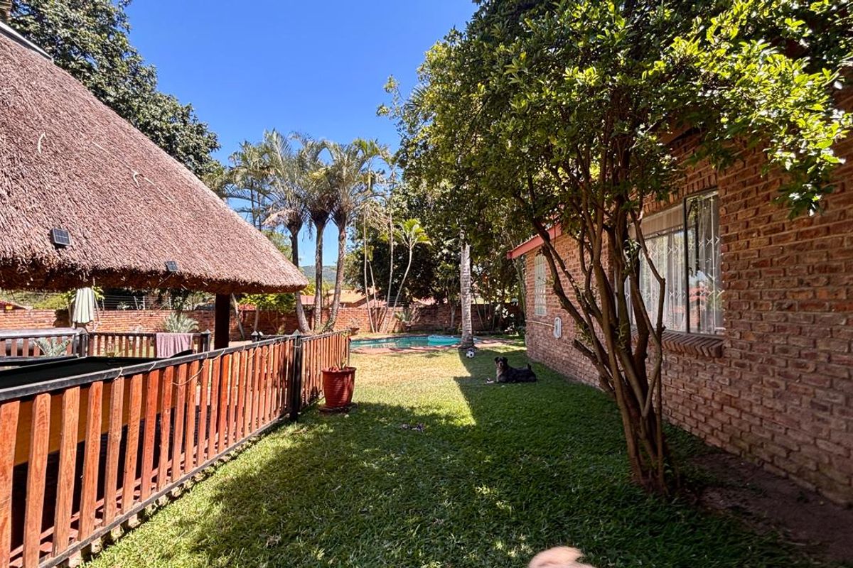 Rear garden area featuring a thatched lapa, swimming pool, and established lawn, bordered by a brick exterior wall and timber fencing.