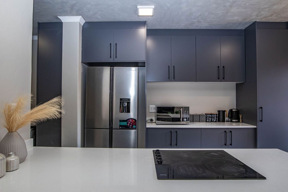 Modern kitchen featuring dark grey cabinetry, white stone countertops, and a built-in electric hob, offering a sleek and functional culinary space.