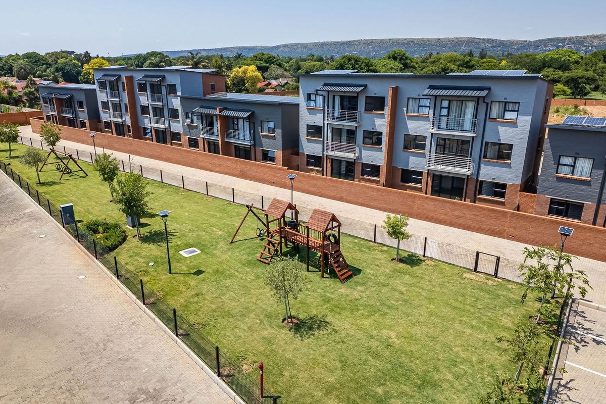 Aerial view of a modern apartment complex featuring a landscaped communal garden, children's play area, and paved parking facilities.