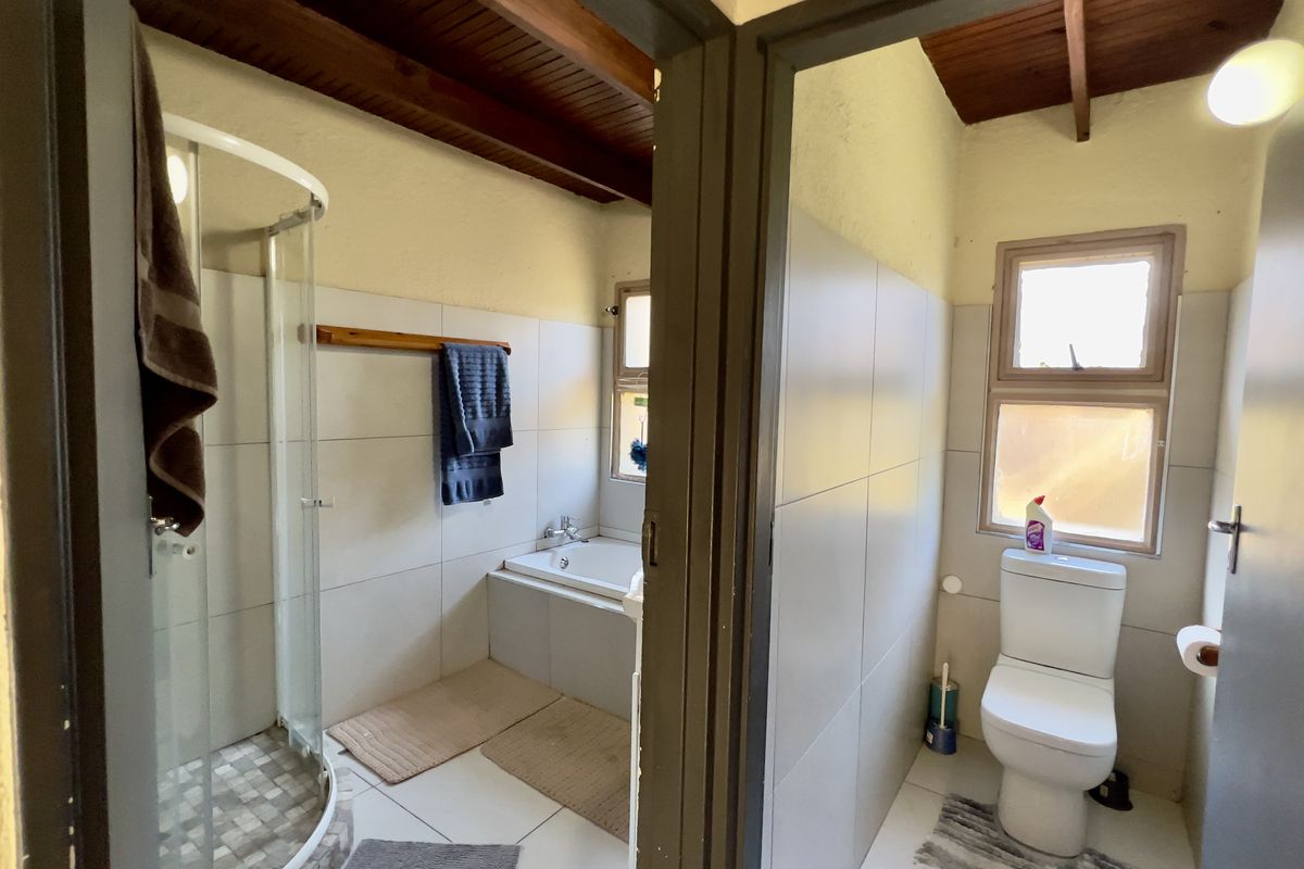 A functional bathroom featuring a separate shower enclosure, built-in bathtub, and toilet, finished with neutral wall tiles and exposed timber ceiling beams.