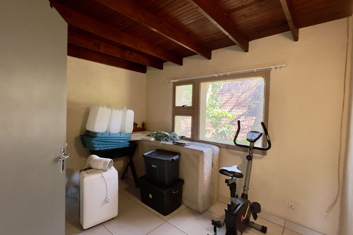 A bedroom featuring exposed timber ceiling beams, tiled flooring, and an aluminium window frame, currently utilized as a storage and exercise space.