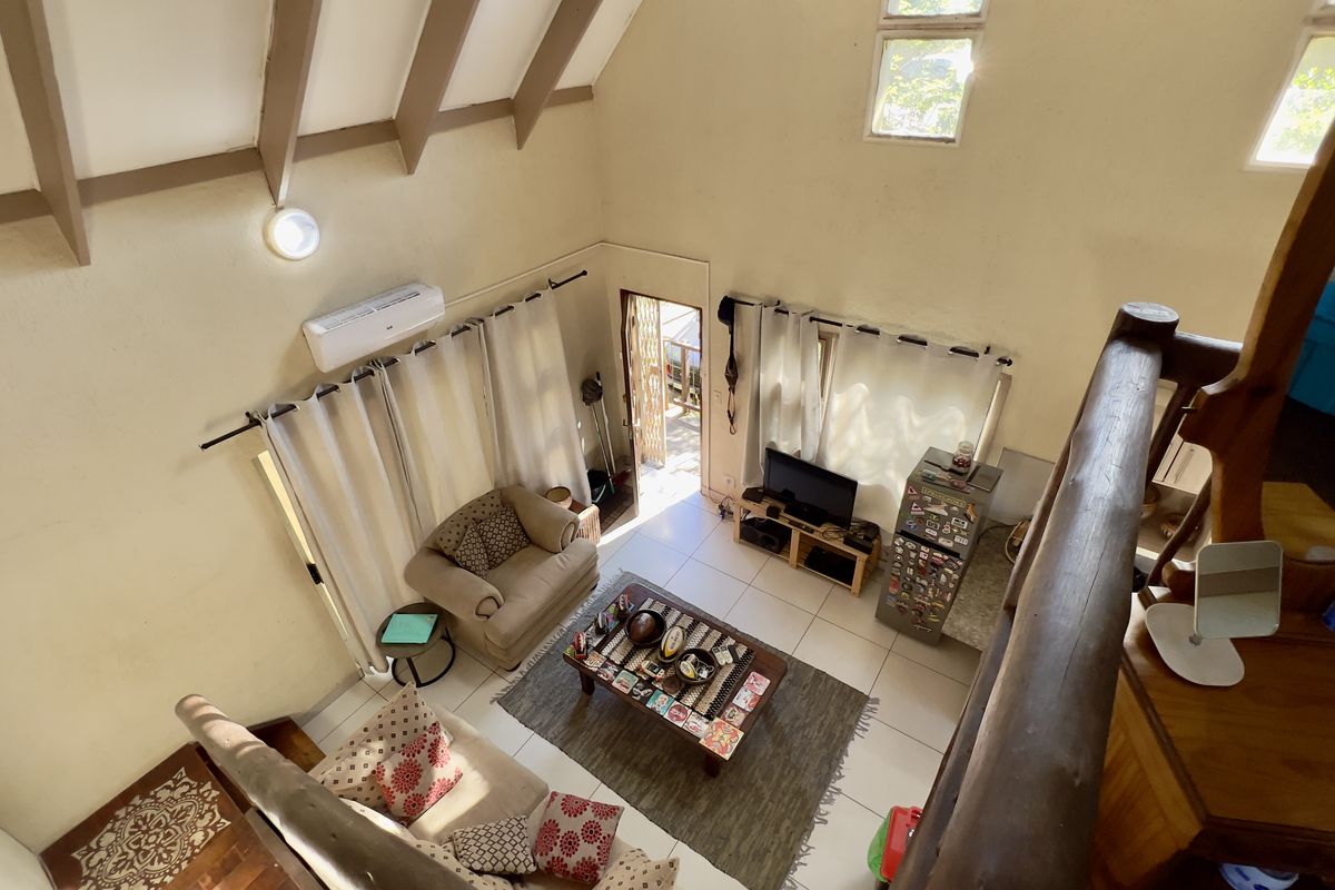 Spacious living area featuring high vaulted ceilings with exposed timber beams, tiled flooring, and a wall-mounted air conditioning unit.