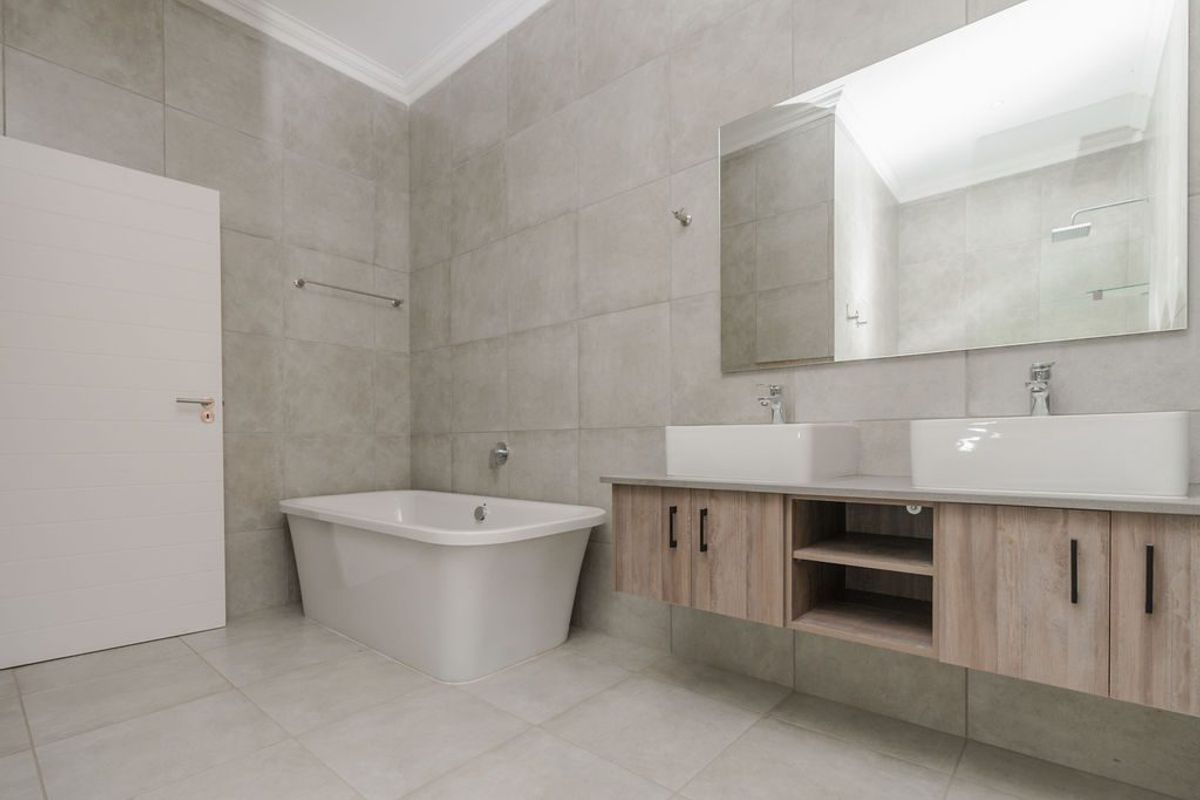 Modern bathroom featuring a freestanding bathtub, double vanity with vessel sinks, wall-mounted cabinetry, and large-format neutral wall and floor tiles.