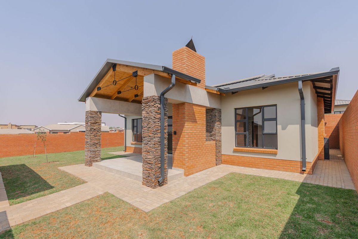 A well-maintained townhouse rear exterior featuring a covered patio with stone-clad pillars, a brick chimney, and a neat garden with paved walkways.
