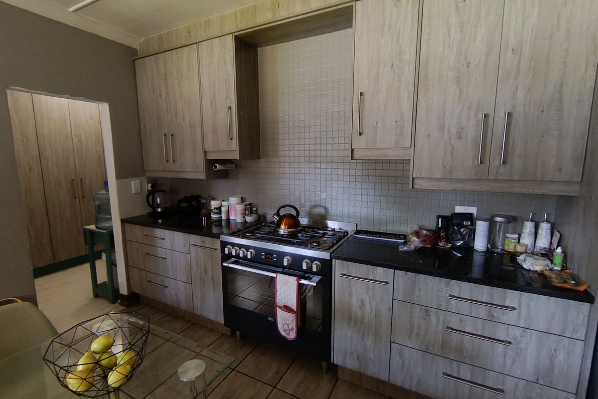 A functional kitchen featuring wood-look cabinetry, dark granite countertops, a gas stove with oven, and a tiled backsplash.