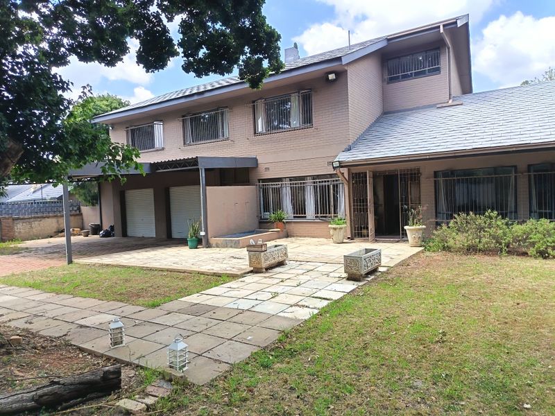 Rear view of a double-story brick house featuring a paved patio area, double garage, and established garden space.