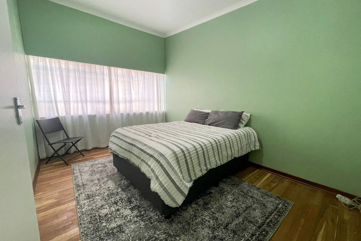 A bedroom featuring hardwood flooring, green painted walls, and a large window with sheer curtains.