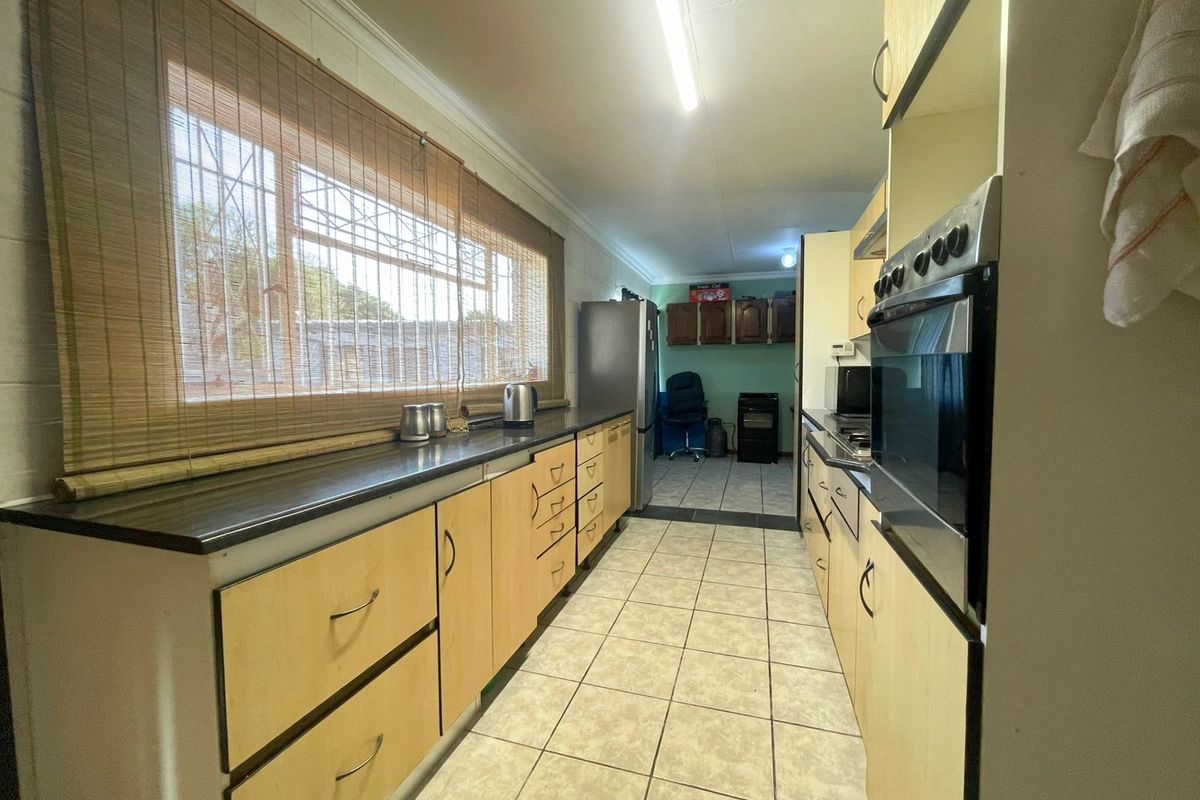 A functional galley-style kitchen featuring light wood-tone cabinetry, dark countertops, built-in oven, and tiled flooring with a window providing natural light.