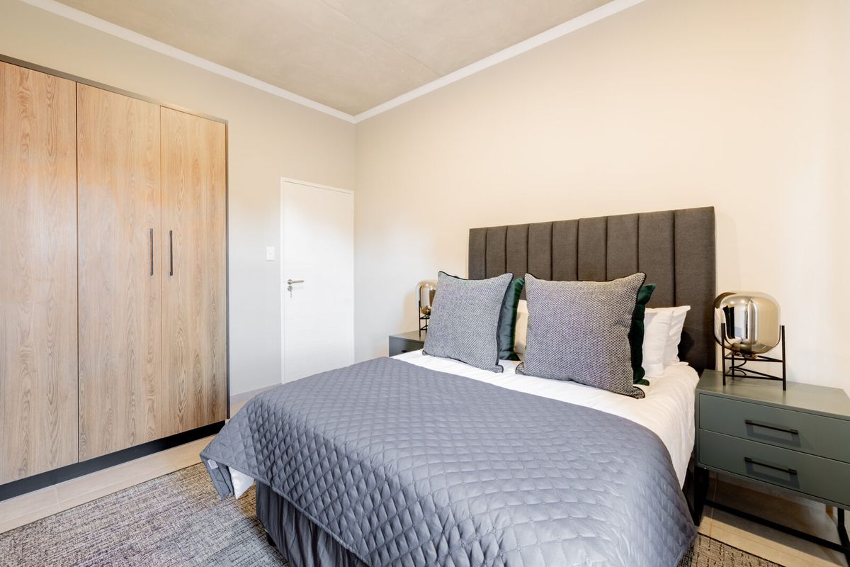 A well-maintained bedroom featuring built-in wooden cabinetry, neutral wall finishes, and a modern concrete-look ceiling.
