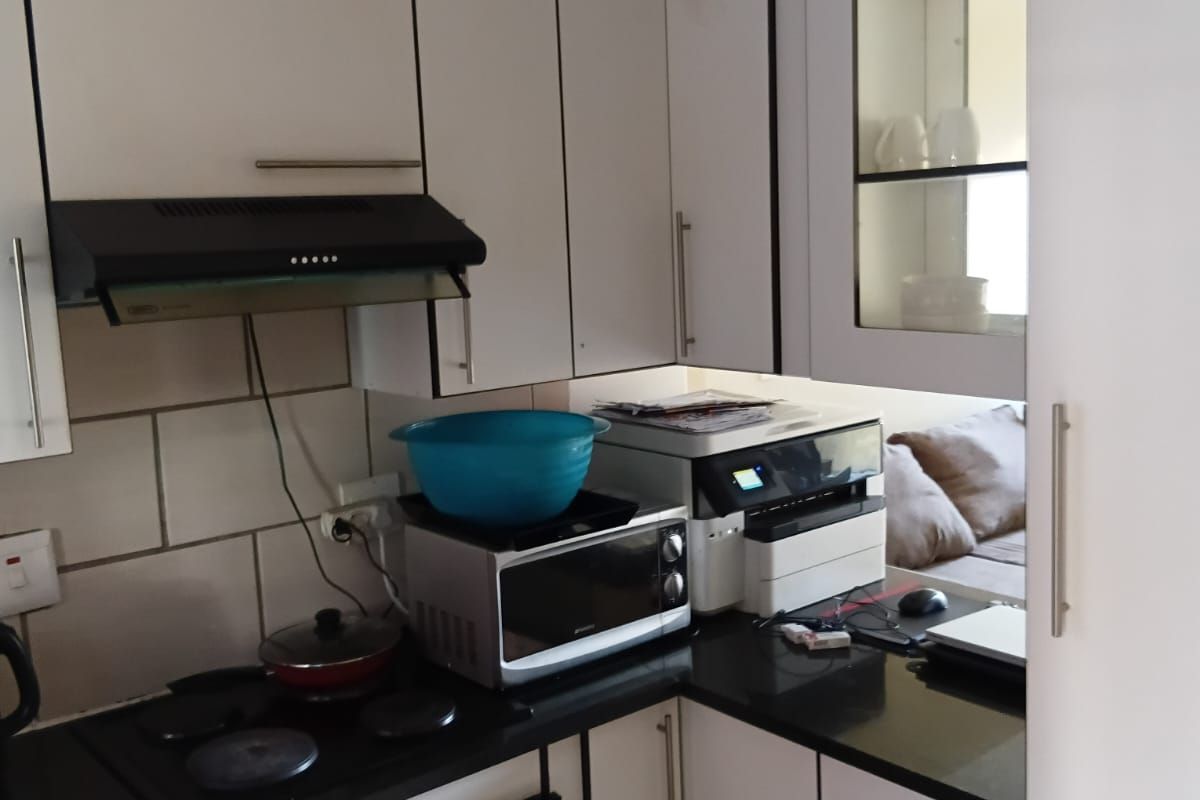 Compact kitchen featuring white cabinetry, black countertops, built-in oven, electric hob, and extractor fan with tiled splashback.
